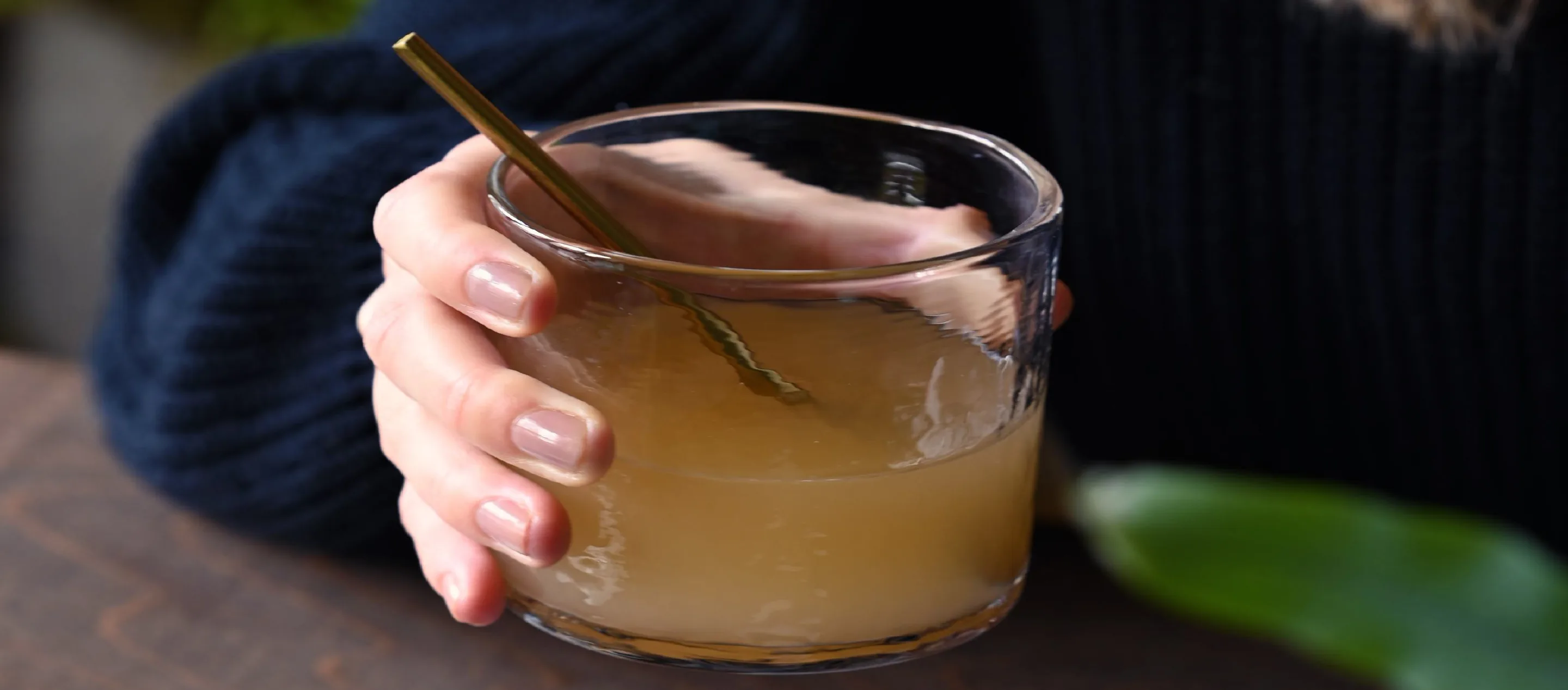A hand holding a glass of Cidrani spritz with a gold stirrer